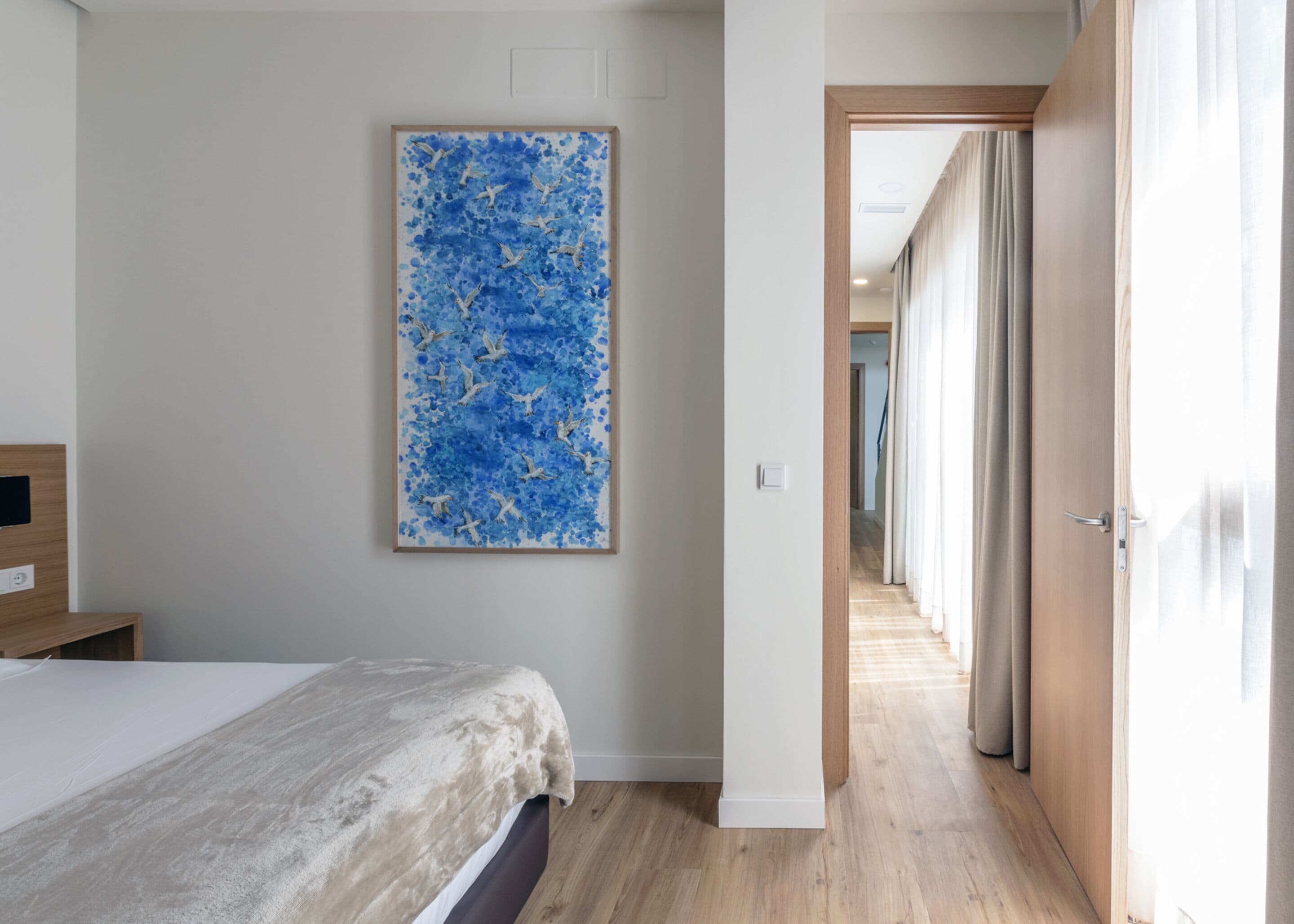 A hotel room with a bed, a wooden headboard, a large abstract painting on the wall, and a hallway leading to another room.