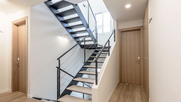 A modern staircase with a glass railing, wooden steps, and a light-colored wall. - Graffiti Suites El Museo (Málaga)