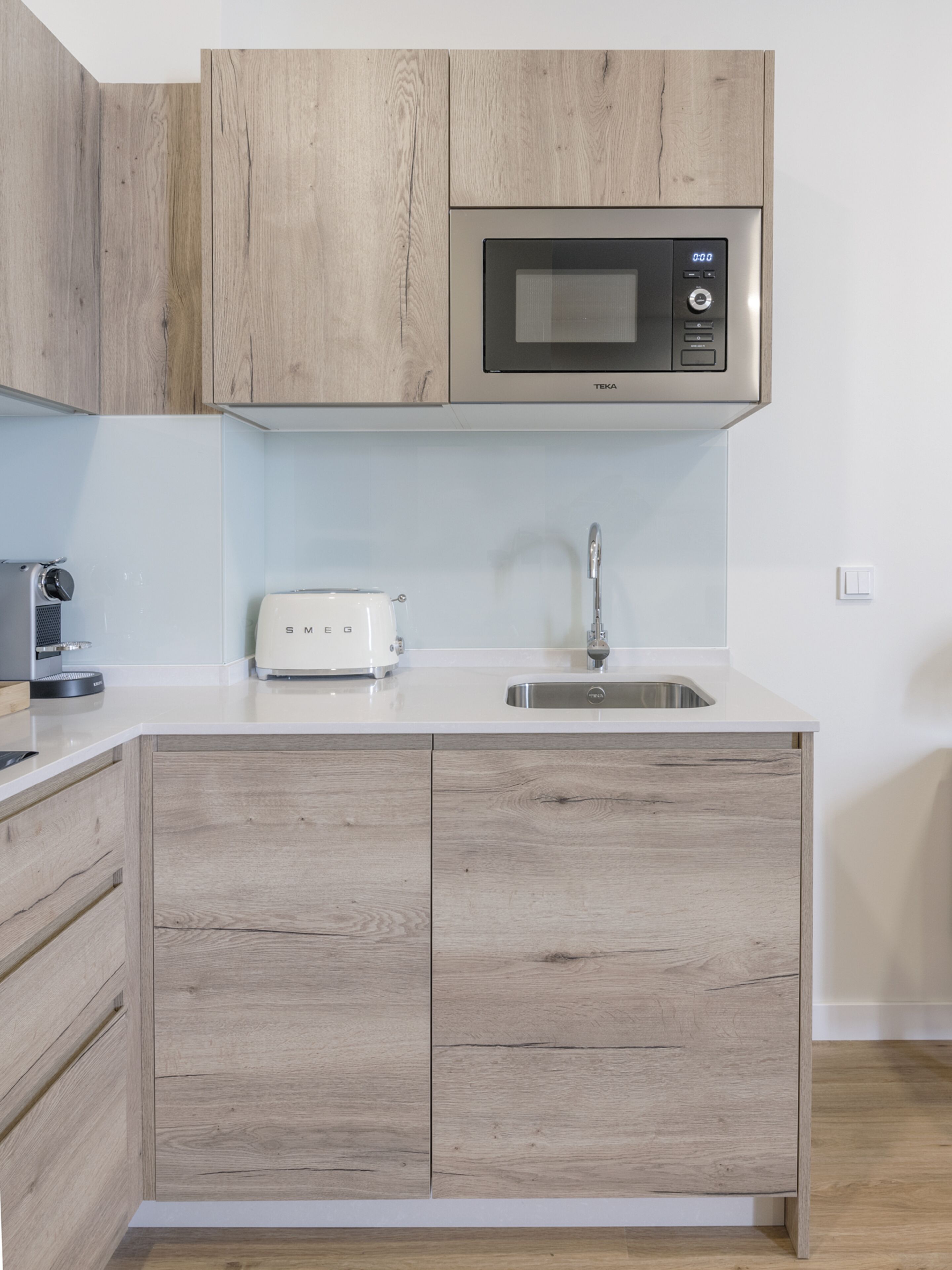 A modern kitchen with wooden cabinets, a built-in microwave, a toaster, and a stainless steel sink.