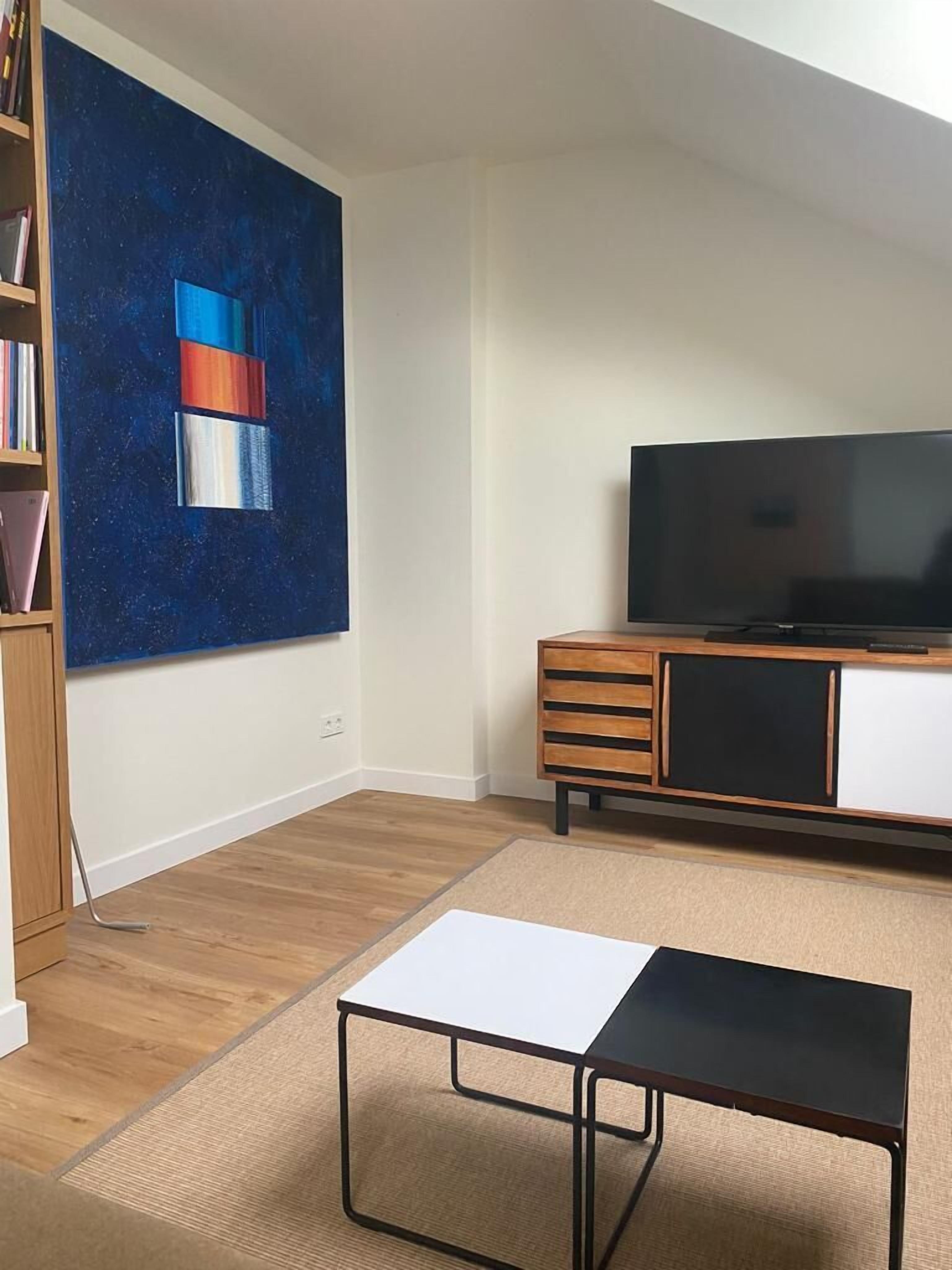 Ein Wohnzimmer mit Flachbildfernseher, Bücherregal, Gemälde und Couchtisch.