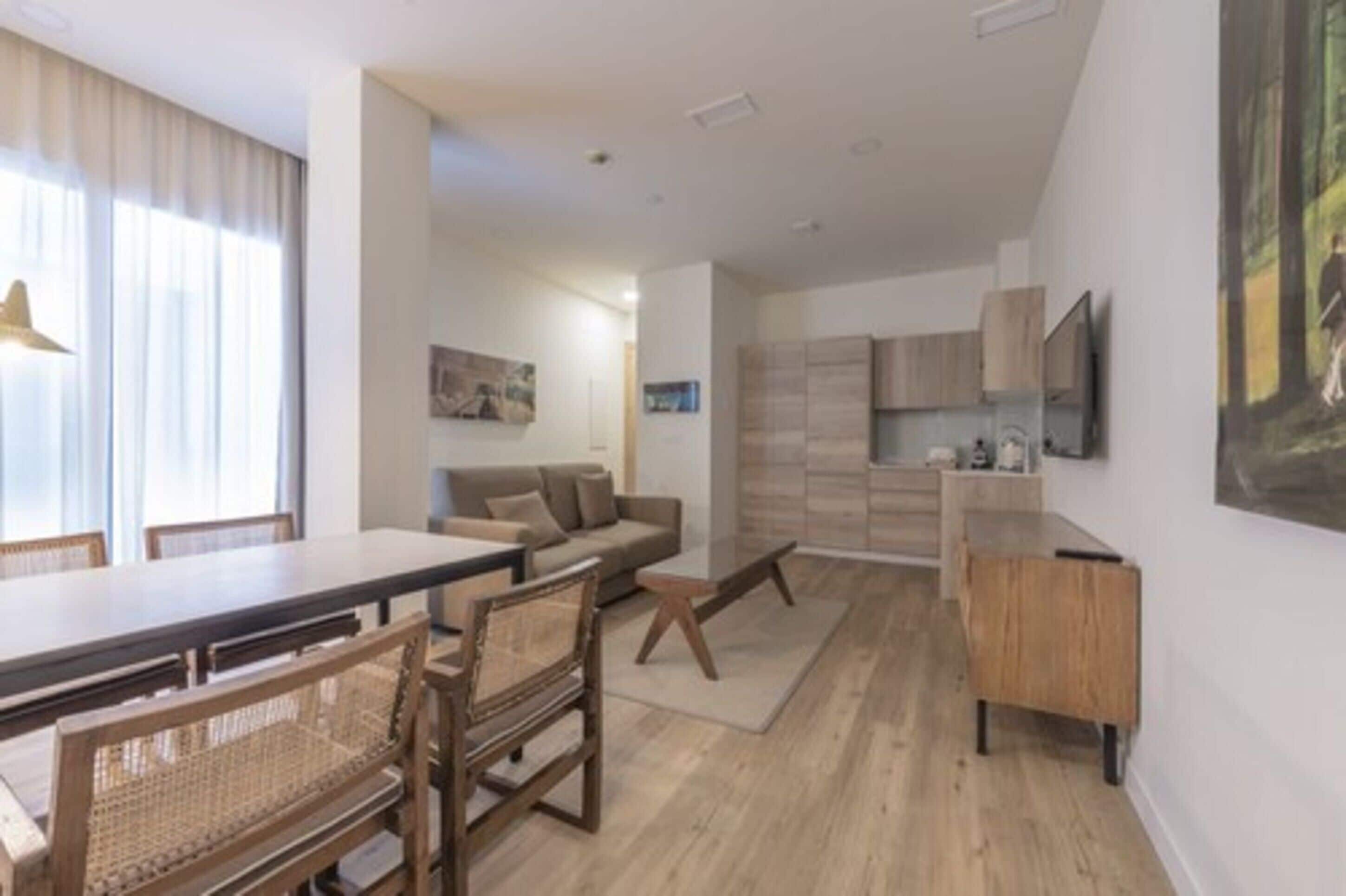 A modern living room with a dining area, a sofa, a TV mounted on the wall, and a wooden cabinet.