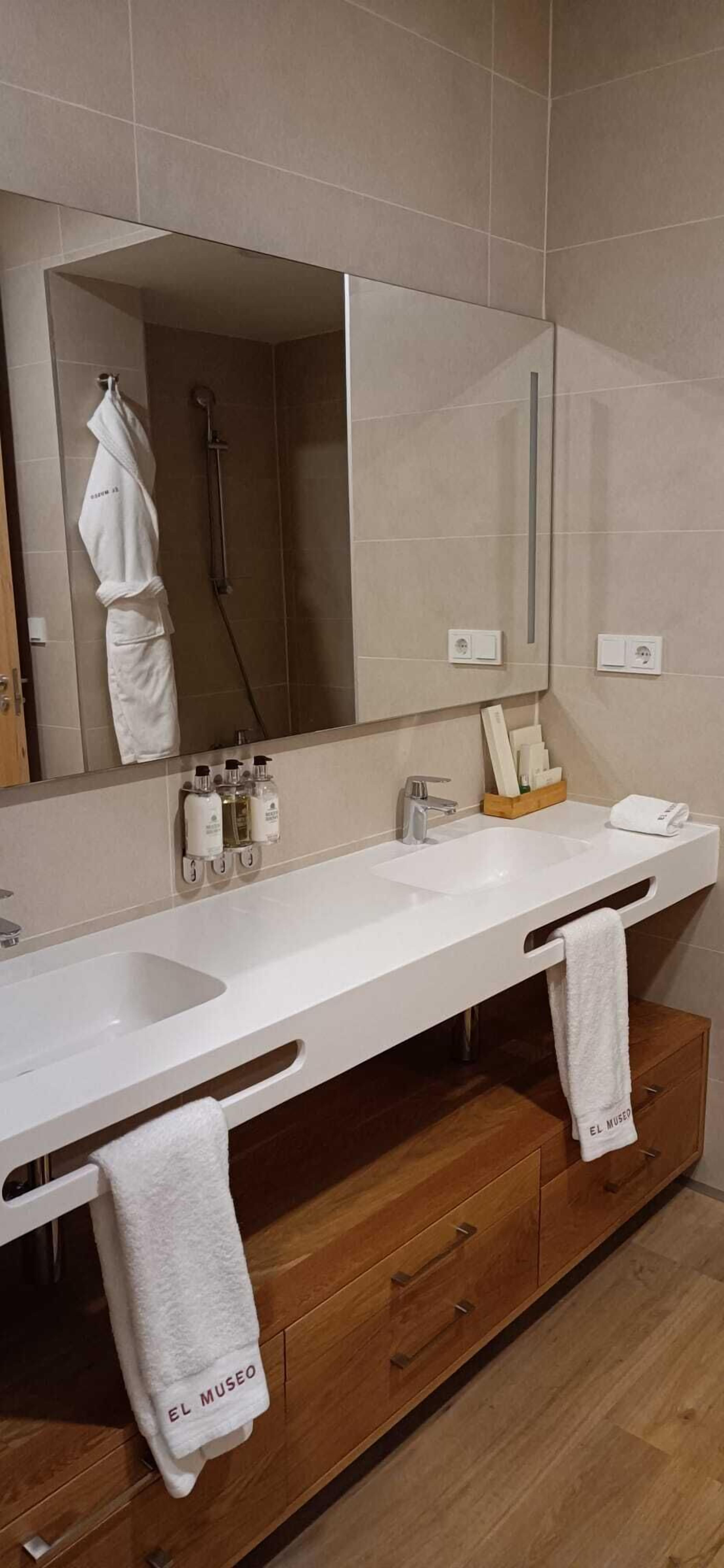 Un baño moderno con un espejo grande, dos lavamanos, una ducha y armarios de madera.
