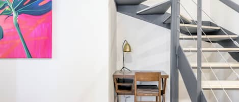 En trappe med et moderne design, et skrivebord med en stol, og et farverigt abstrakt maleri på væggen.