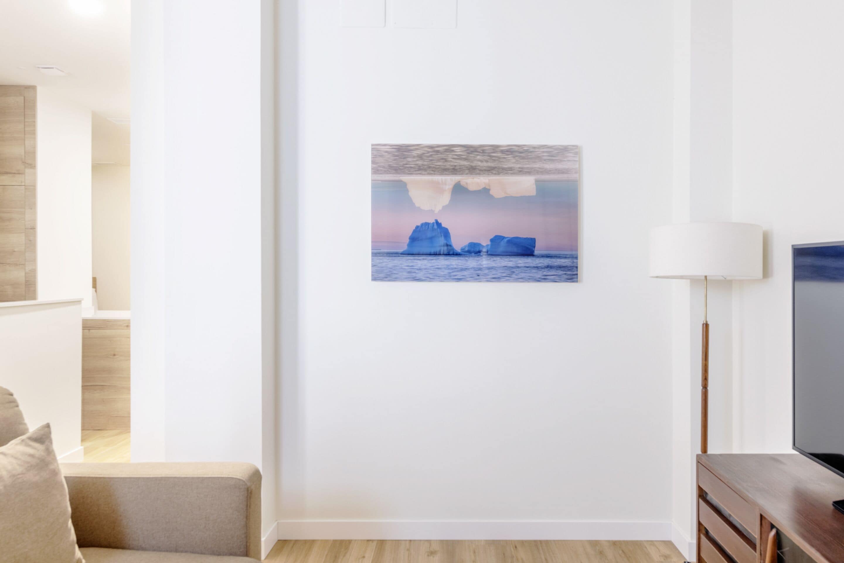 Una sala de estar con un cuadro de icebergs, un sofá, una lámpara y un televisor sobre un soporte de madera.