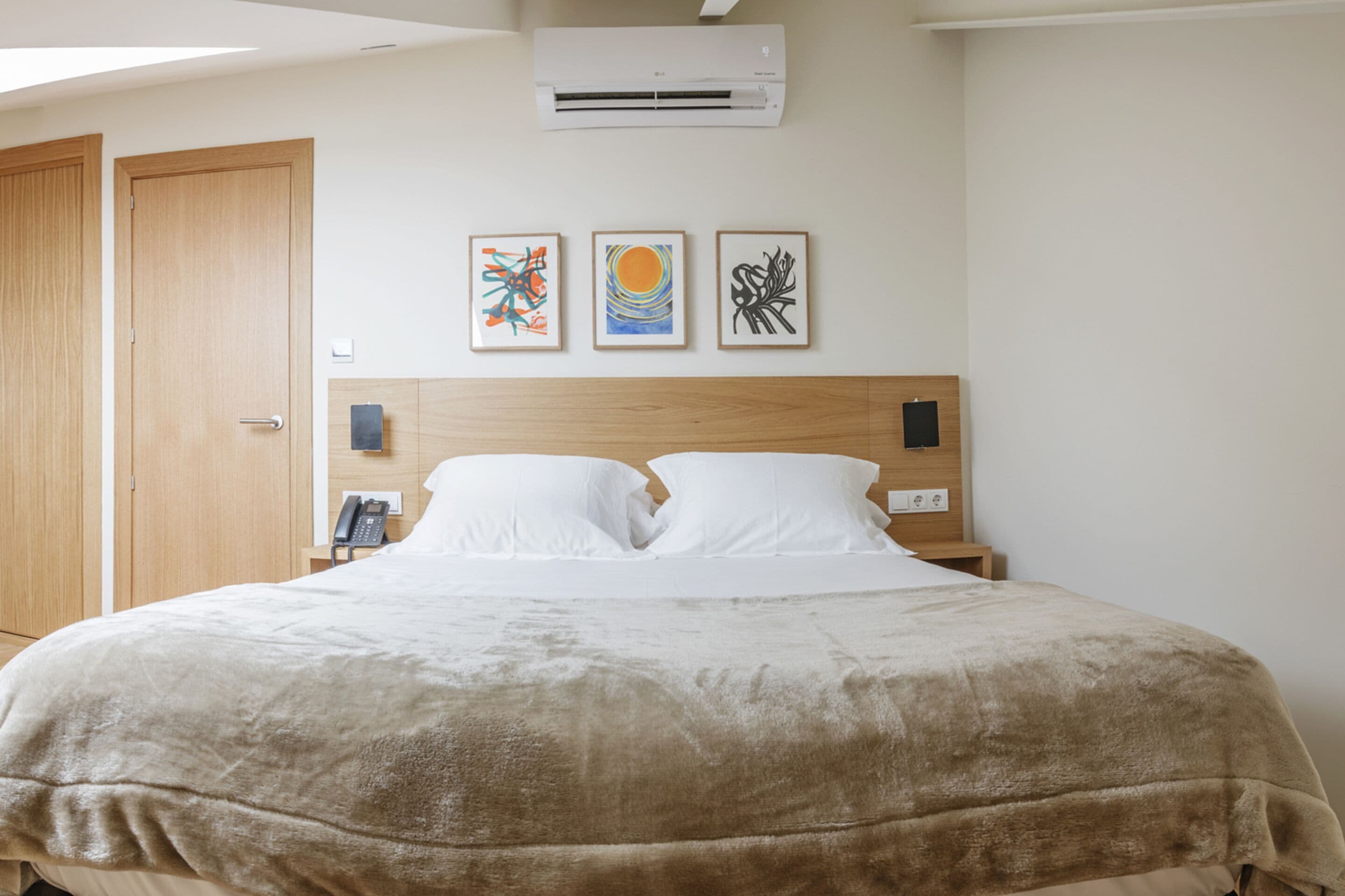 A hotel room with a large bed, a wooden headboard, and three framed artworks on the wall.