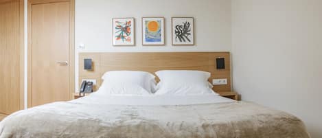 A hotel room with a large bed, a wooden headboard, and three framed artworks on the wall.