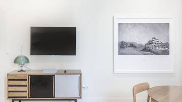 Una sala de estar minimalista con un televisor de pantalla plana montado en la pared, un mueble de madera con cajones, una lámpara de escritorio verde y una fotografía en blanco y negro enmarcada en la pared.