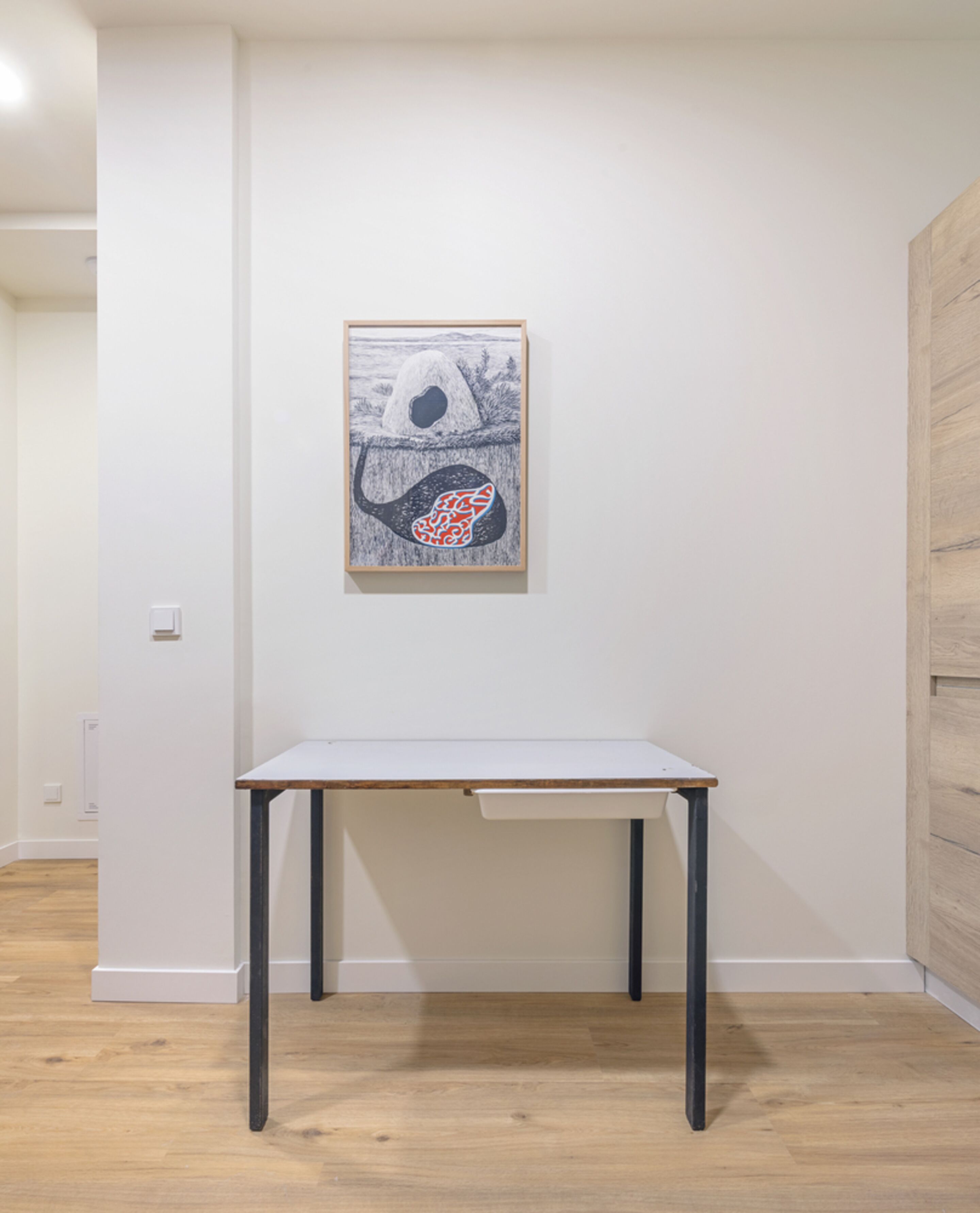 Une pièce au décor minimaliste, avec une table blanche, une œuvre d’art encadrée au mur et un plancher en bois.