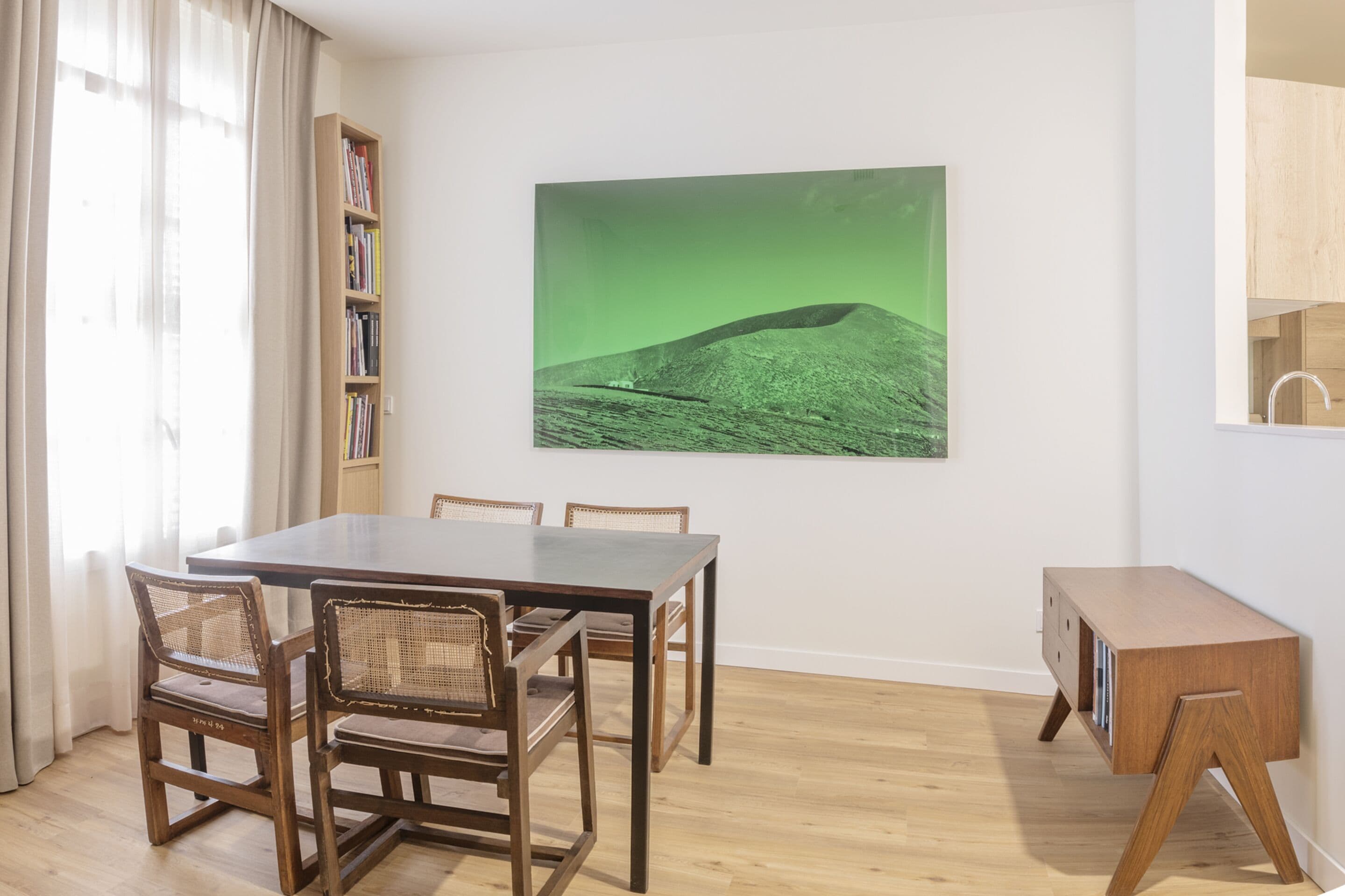 Ein Essbereich mit einem Holztisch und Stühlen, einem Bücherregal und einem grünen Landschaftsgemälde an der Wand.