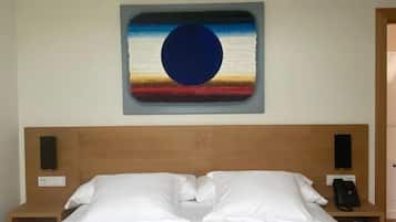 A hotel room with a large bed, a wooden headboard, a wall-mounted painting, bedside tables with lamps, and a telephone.