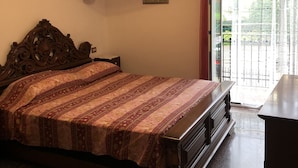Un dormitorio con una cama grande, cabecera de madera, lámpara colgante, un cuadro enmarcado en la pared y vistas al exterior a través de una puerta de cristal.