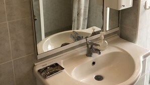 Un baño con cabina de ducha de vidrio, un lavamanos blanco con dispensador de jabón y un espejo sobre el lavamanos.