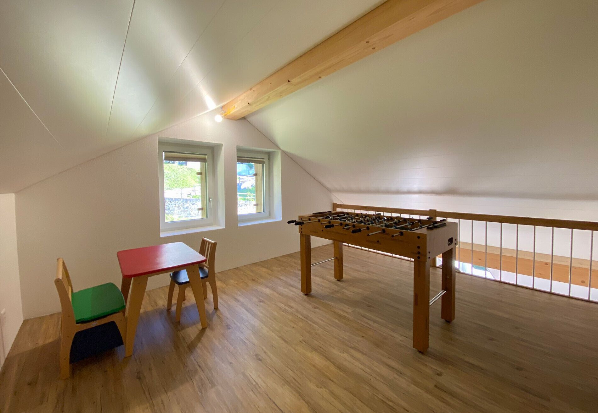 Een kamer met een houten tafelvoetbaltafel, een rode tafel en twee stoelen met groene en blauwe kussens.