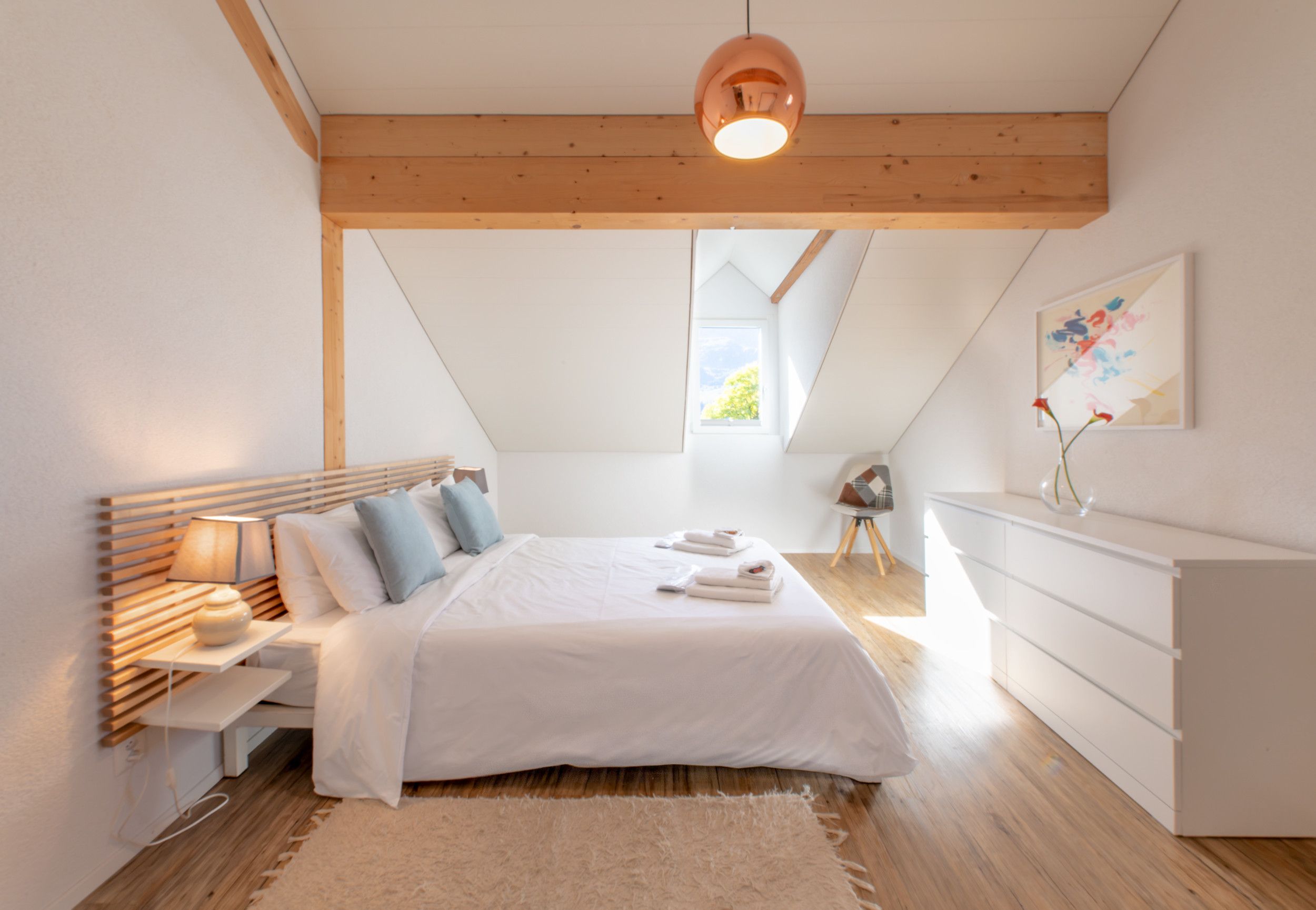 Un dormitorio con cama, mesita de noche, lámpara, cómoda y un cuadro en la pared.