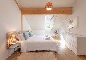 Een slaapkamer met een bed, nachtkastje, lamp, dressoir en een schilderij aan de muur.
