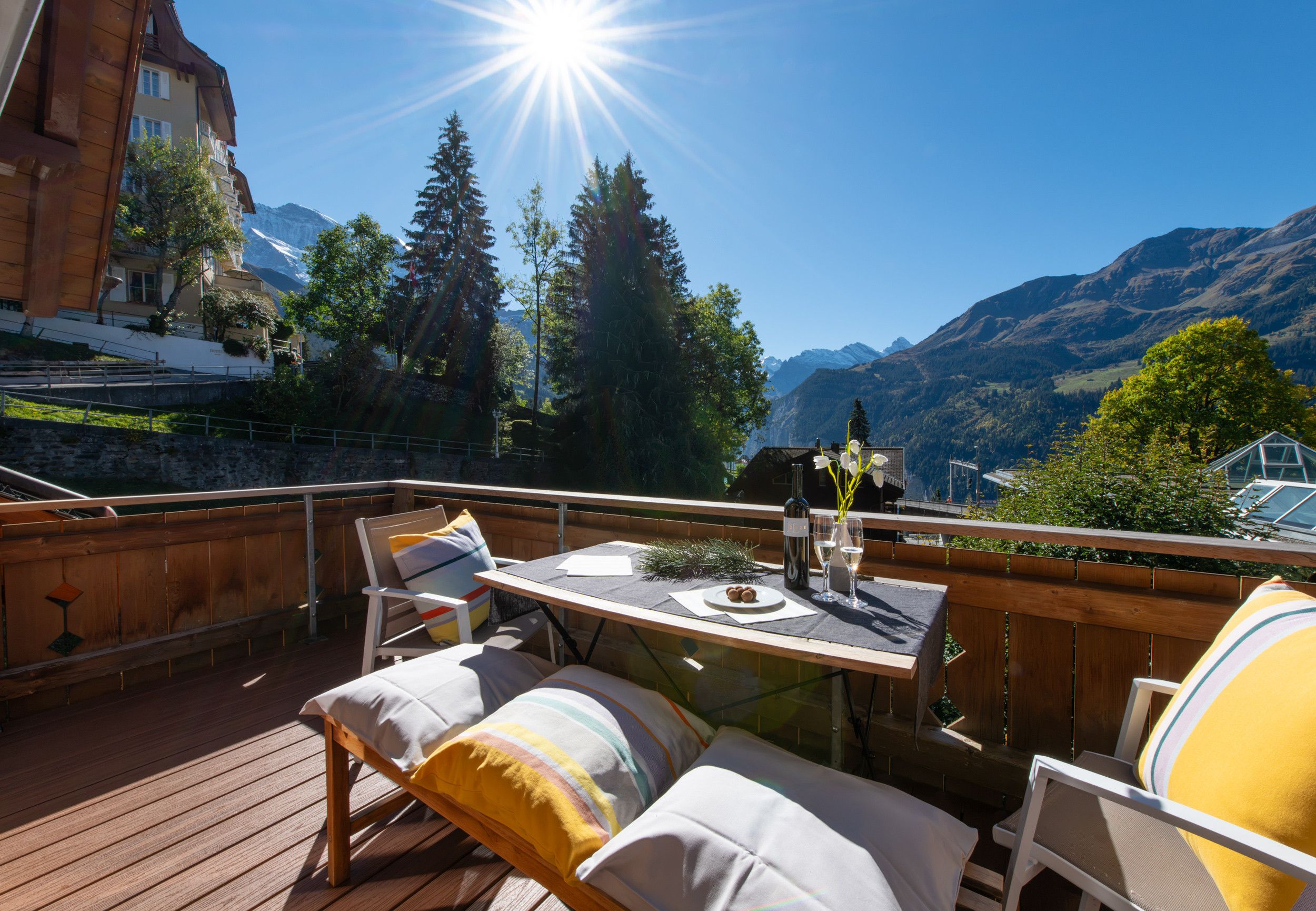 Una terraza de madera con mesa y sillas, con vistas a un paisaje montañoso.
