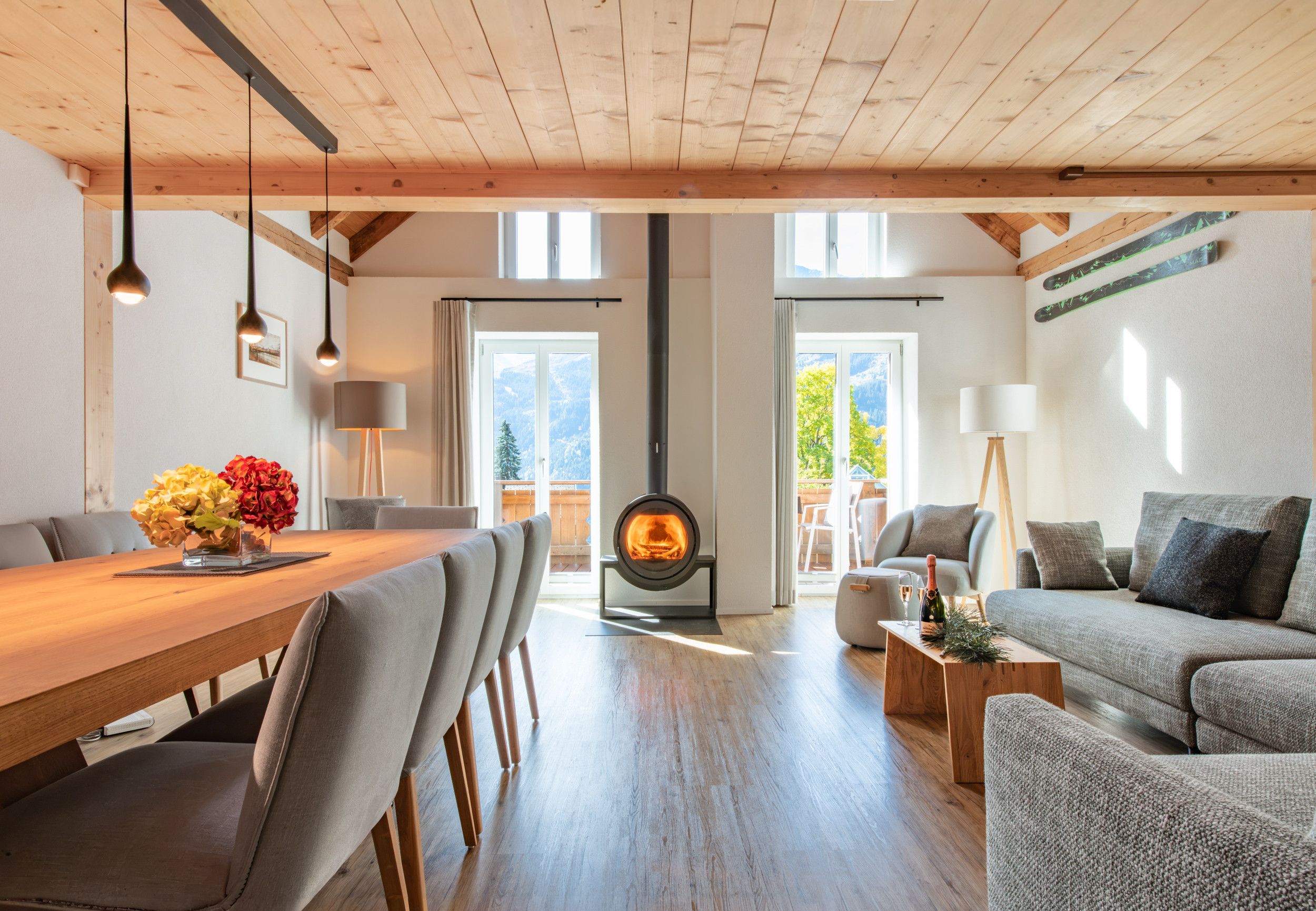 A spacious living area with a wooden ceiling, a central fireplace, and a dining area with a wooden table and chairs.