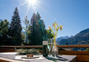 Une table avec une bouteille, des verres et une assiette de nourriture, le tout placé devant un paysage de montagne.