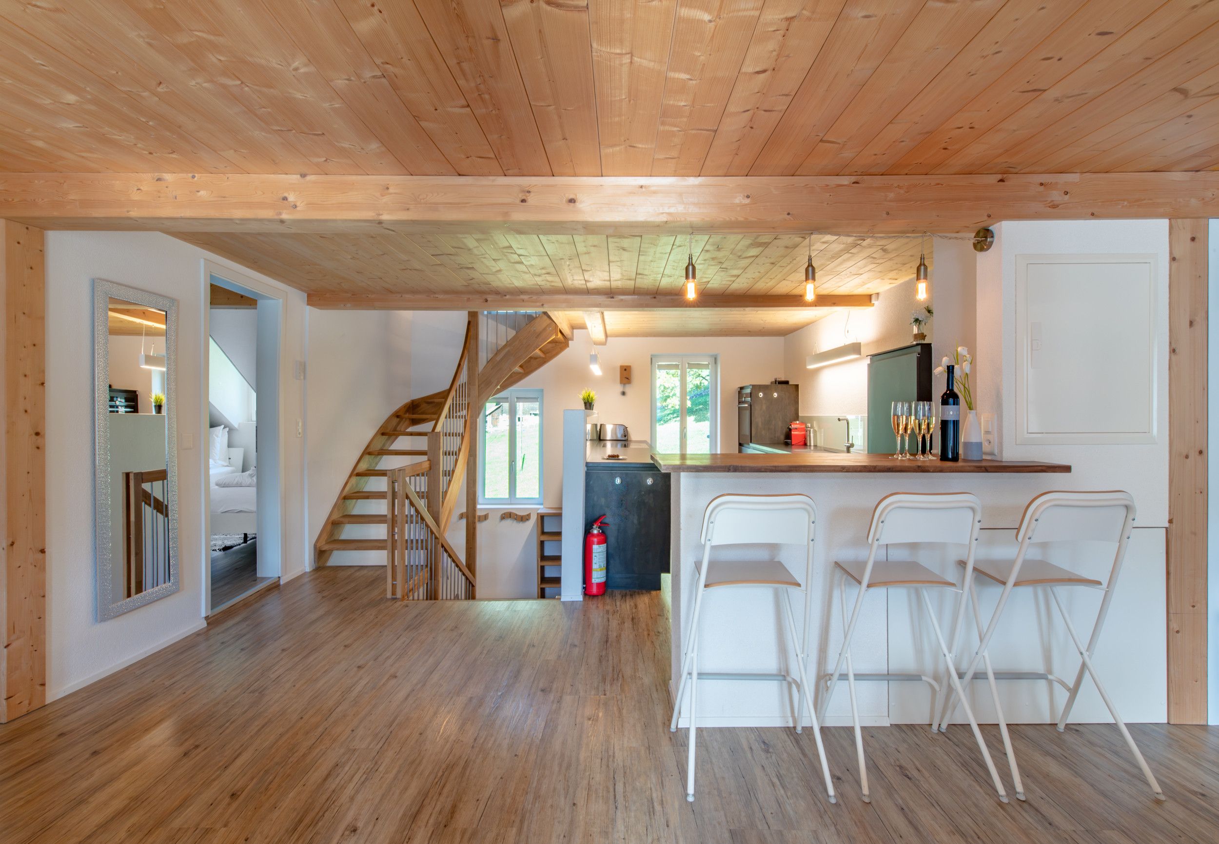 Una cocina amplia con techo de madera, estufa integrada y zona de bar con sillas blancas.