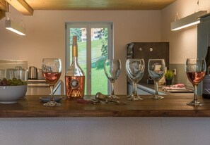 A kitchen counter with a bottle of wine, glasses, and a bowl of grapes. - Le Manoir Penthouse - spacious, new and central location (Wengen)