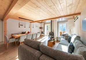 Un vaste espace de vie doté d’un plafond haut, de poutres apparentes, d’une table à manger pour quatre personnes et d’un coin salon confortable.
