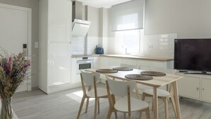 A modern kitchen with white cabinetry, a dining table with chairs, and a flat-screen TV. - Two bedroom apartment with garden - DDS ONS (Vigo)