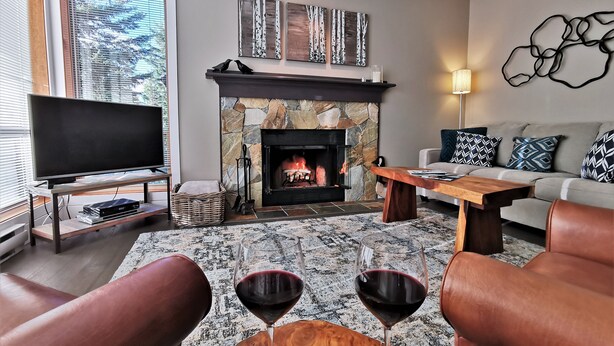 A living room with a stone fireplace, a flat-screen TV, leather sofas, and a coffee table with wine glasses.