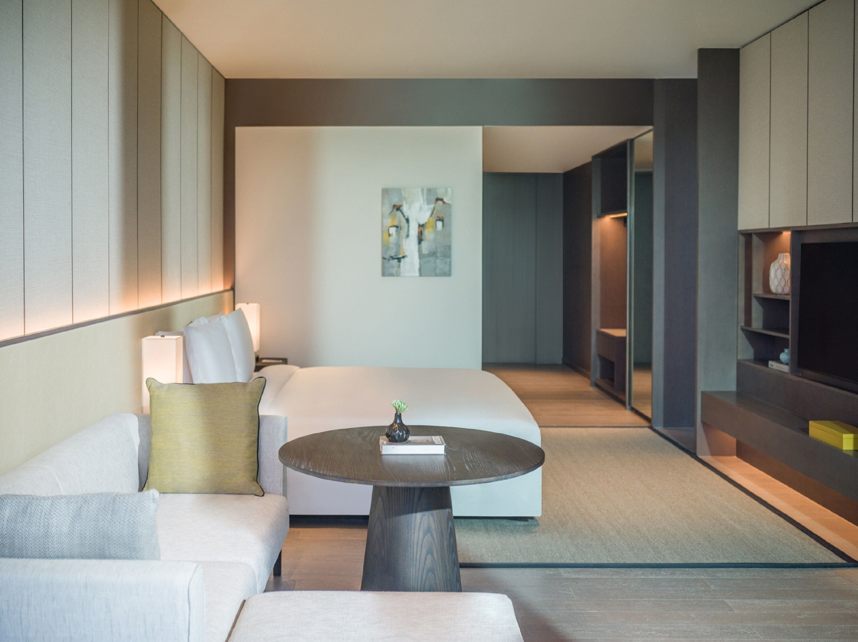 A modern hotel room with a sofa, a round coffee table, and a bed.