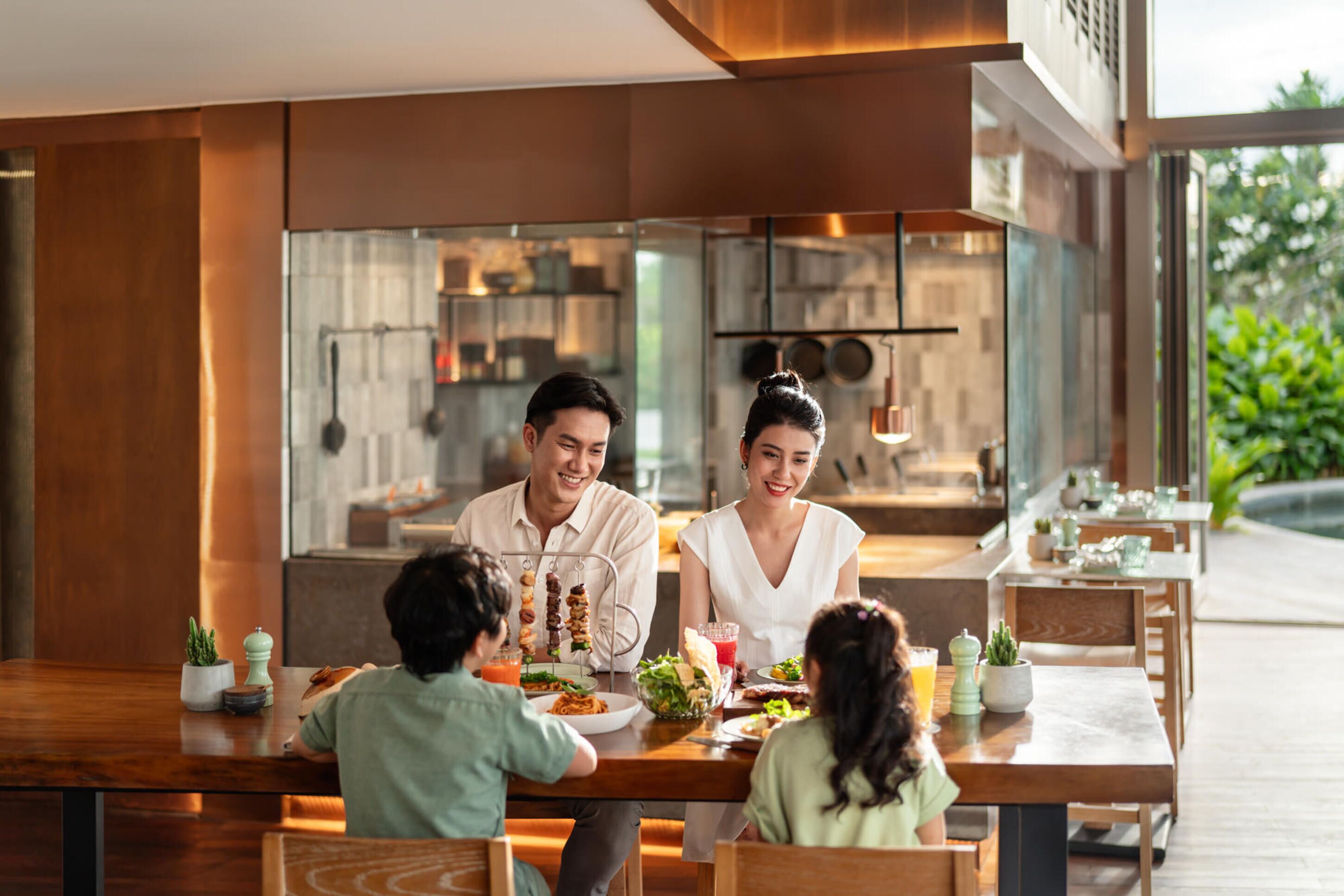 Una familia cenando en un restaurante con una decoración moderna, ventanas amplias y una zona de cocina a la vista.