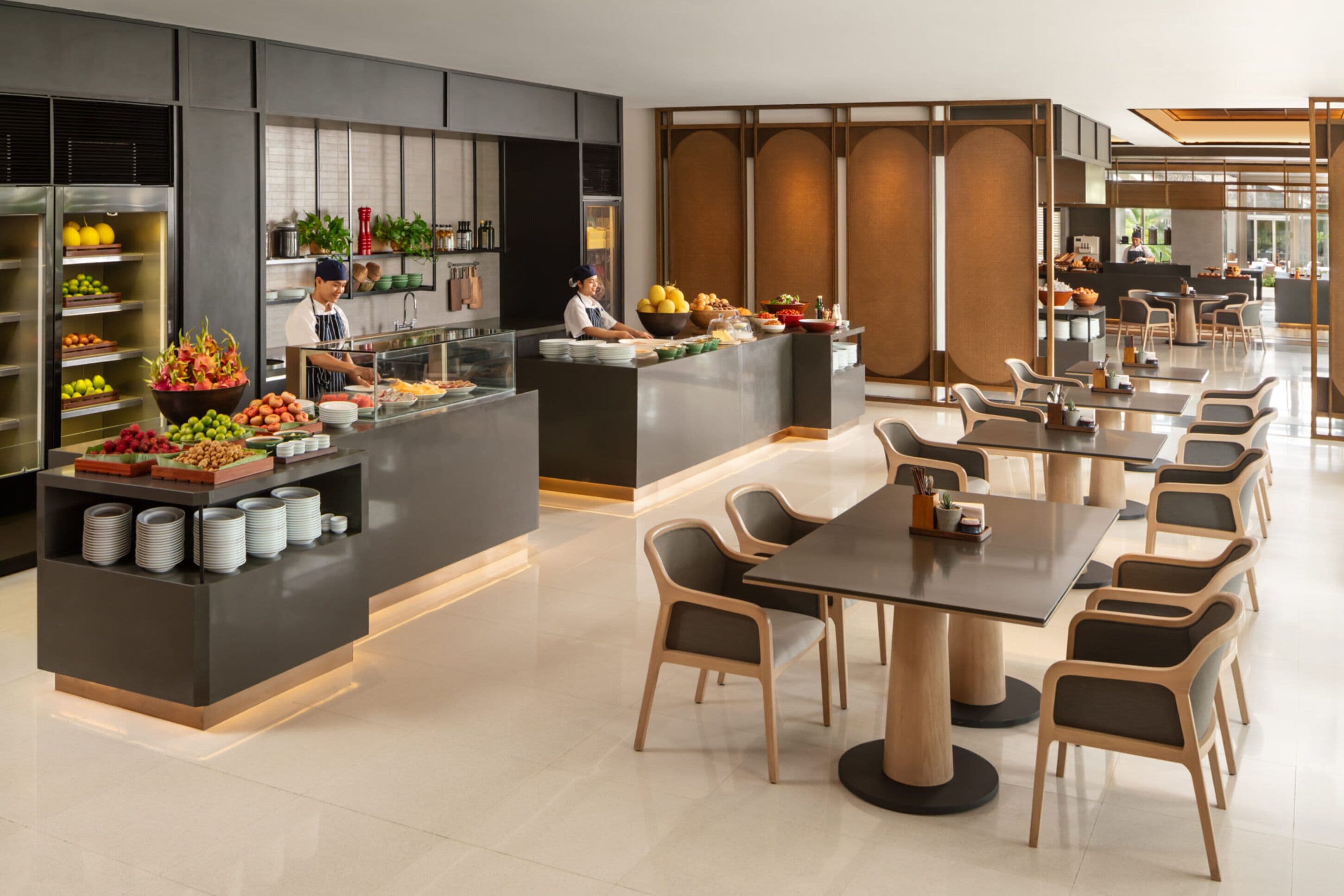 A modern restaurant with a buffet area, multiple dining tables, and a chef preparing food.
