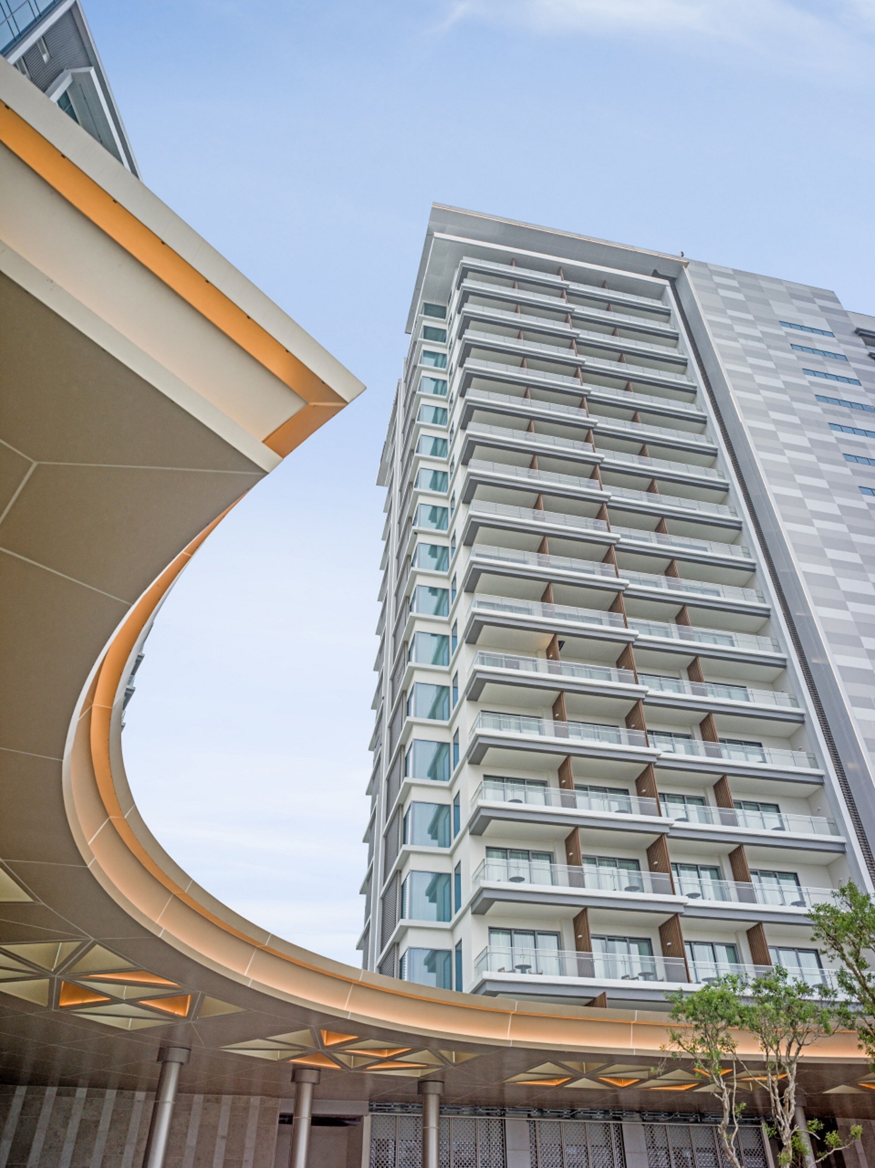 A modern high-rise building with a curved entrance canopy and multiple balconies.
