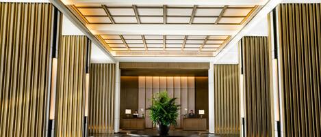 A modern lobby with a checkered floor, a central plant, and vertical wooden panels.