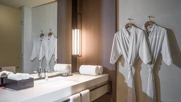 Un baño moderno con un espejo grande, paneles de madera, un lavamanos blanco y dos albornoces colgados en un perchero.