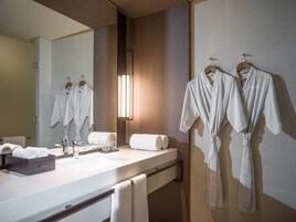 Un baño moderno con un espejo grande, paneles de madera, un lavamanos blanco y dos albornoces colgados en un perchero.
