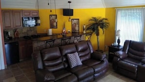 A living room with a brown leather sofa and a dining area with a kitchen in the background. - Home AWAY FROM HOME!!! Franklin, VA<br>(1 BEDROOM) (Franklin)
