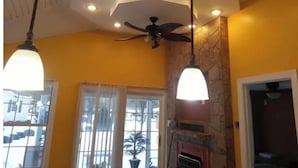 A room with a stone fireplace, a ceiling fan, and two pendant lights. - Home AWAY FROM HOME!!! Franklin, VA<br>(1 BEDROOM) (Franklin)
