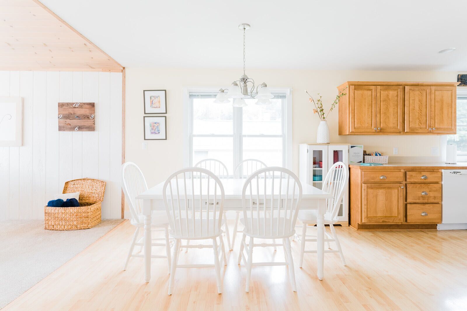 A bright kitchen with wooden cabinets, a white dining table with chairs, and a window with natural light.
