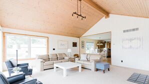 A spacious living room with a high ceiling, a sofa set, a coffee table, and a kitchen visible through an open doorway. - Treloar Lakeside Cottage (Allegan)