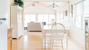 A bright kitchen with white cabinets, a wooden dining table, and chairs. There is a hanging light fixture above the table. - Treloar Lakeside Cottage (Allegan)