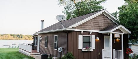 Une petite maison de plain-pied, dotée d’un porche, d’une antenne parabolique et offrant une vue sur un lac.