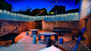 An outdoor patio area with stone walls, wooden tables, and benches. - La Boutique Espacio Rural (Rural, Gastronomic, Playful Experiences, etc ...) (Nuévalos)