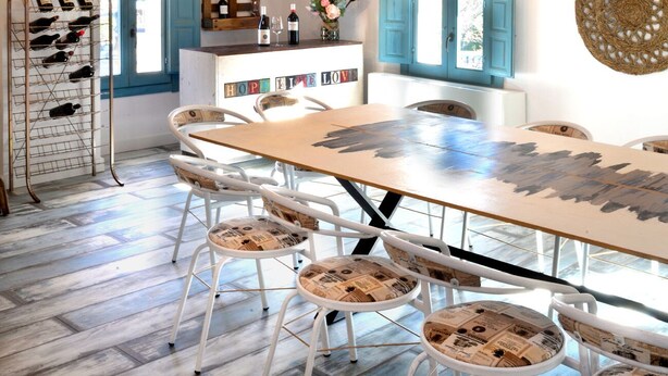 A rustic dining area with a wooden ceiling, a long table, and white chairs with newspaper seat covers. - La Boutique Espacio Rural (Rural, Gastronomic, Playful Experiences, etc ...) (Nuévalos)