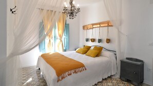 A bedroom with a bed, a chandelier, a nightstand, and a window with curtains. - La Boutique Espacio Rural (Rural, Gastronomic, Playful Experiences, etc ...) (Nuévalos)