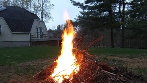 A campfire in a backyard with a house and trees in the background. - Quiet Waterfront Home (Waddington)