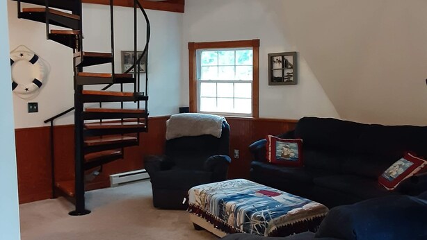 A spacious loft with a high ceiling, a spiral staircase, a large window, and a cozy seating area with a sofa and ottoman. - Quiet Waterfront Home (Waddington)