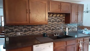 A kitchen with wooden cabinets, a tiled backsplash, a dishwasher, and a sink. - Quiet Waterfront Home (Waddington)