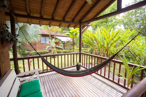 Relax in a hammock suspended between two posts, surrounded by lush greenery and a wooden bench with cushions.