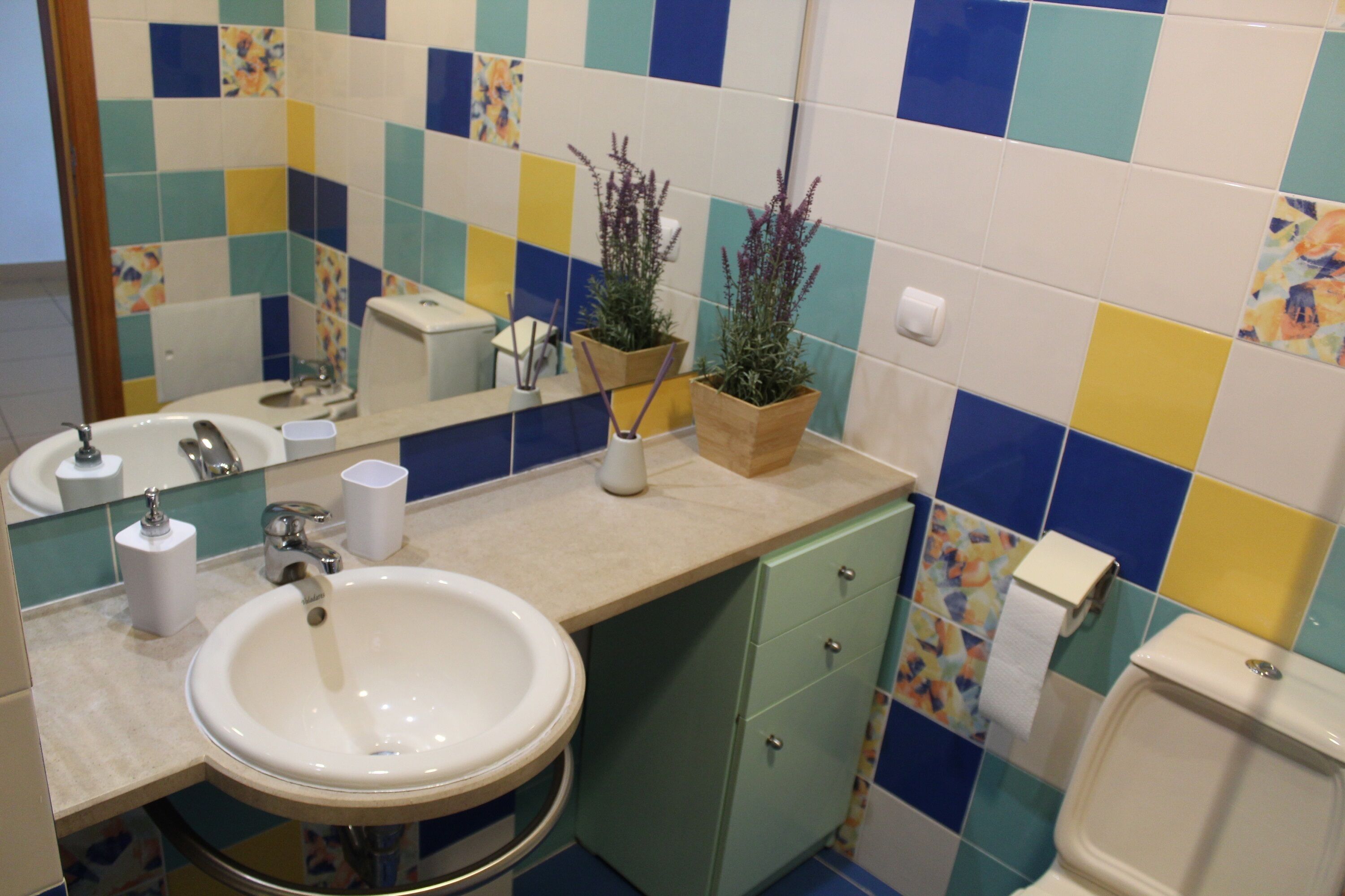 A bathroom with a sink, mirror, toilet, and decorative tiles.