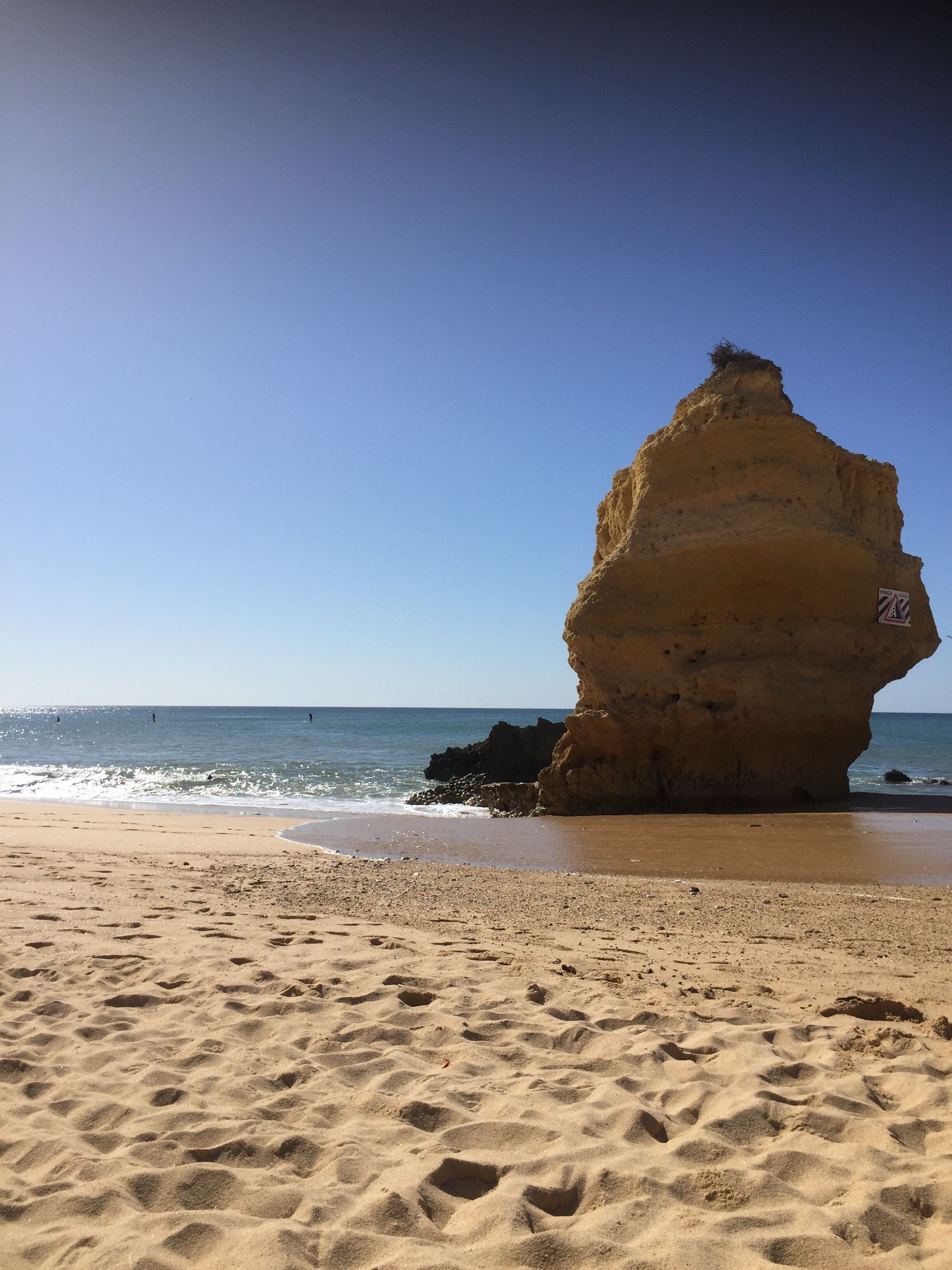 A sandy beach with a large rock formation and a warning sign.