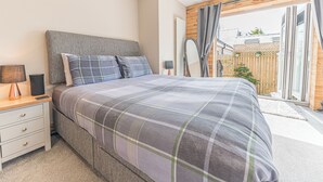 A modern bedroom with a large bed, a bedside table with a lamp, and a view of the outside. - 1 bedroom accommodation in Ulverston (Ulverston)